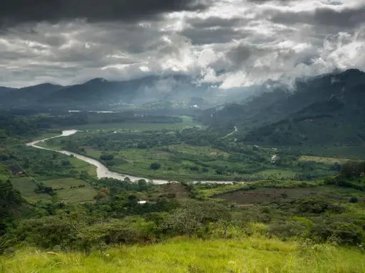 Ein gewundener Fluss schlängelt sich durch ein grünes Tal in Costa Rica. Wolken ziehen über die Berge, die das Bild umrahmen.