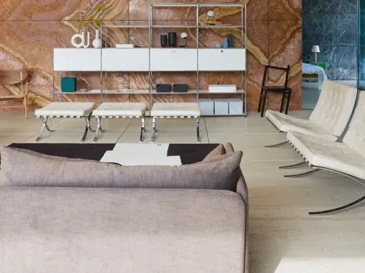 Soggiorno moderno con divano grigio, poltrone in pelle bianca e sgabelli, su sfondo di travertino rosso. Il **case design** è elegante e funzionale.