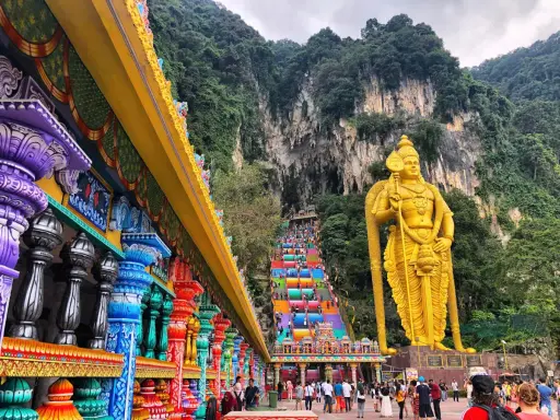 Kolorowe schody Batu Caves w Malezji, prowadzące do jaskini, obok złotej statuy boga Murugana. Warto zobaczyć!