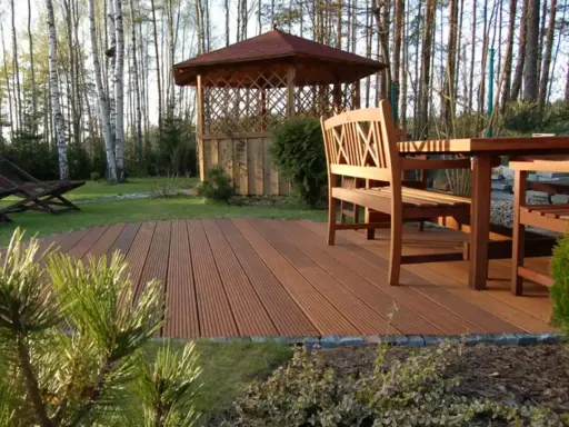 Drewniany taras z meblami i altaną w ogrodzie. Świetny pomysł na tani taras, który doda uroku Twojej przestrzeni.