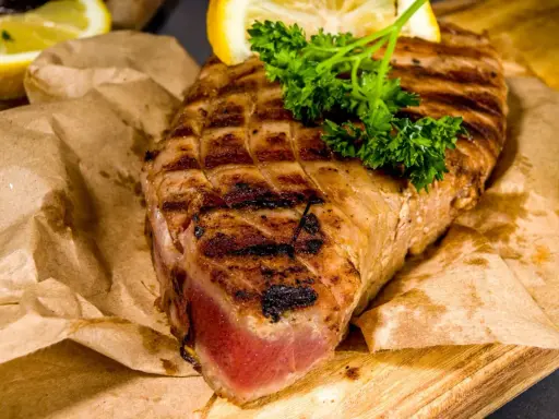 Saftiges Thunfischsteak, perfekt gegrillt, mit Zitronenspalten und Petersilie garniert, auf Packpapier serviert.