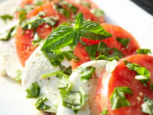 Salade Caprese : fines tranches de tomates rouges et de mozzarella crémeuse, parsemées de basilic frais. Une recette simple et savoureuse.