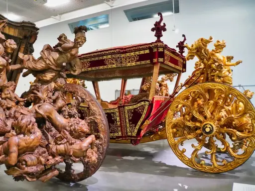 Prunkvolle Kutschen im Kutschenmuseum Lissabon: Eine aus Holz geschnitzte, die andere golden verziert, beide mit aufwendigen Figuren.