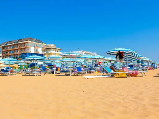 Słoneczny dzień na plaży w Lido di Jesolo. Rzędy leżaków i parasoli w niebiesko-białe pasy czekają na plażowiczów.
