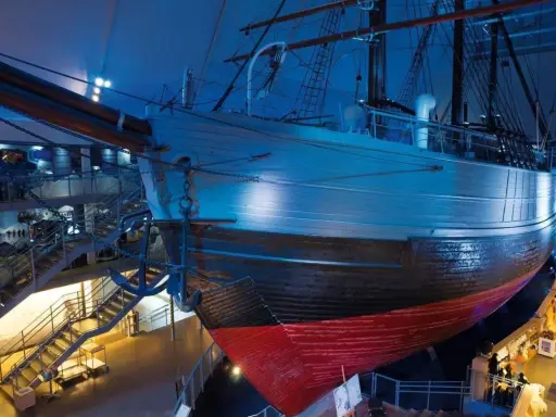 Ein historisches **fram schiff** mit Anker, umgeben von Treppen und Ausstellungsbereichen, in blauem Licht.