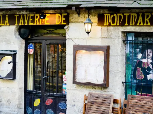 La taverne de Montmartre, une définition de l'ambiance parisienne. Façade de pierre, enseigne jaune, menu affiché, et une peinture murale d'un mousquetaire.