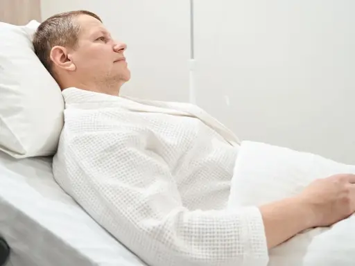 Mężczyzna w białym szlafroku leży w szpitalnym łóżku, przygotowując się do usunięcia pęcherza moczowego.