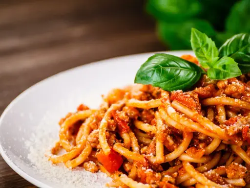 Pyszne spaghetti z bogatym sosem mięsnym, posypane parmezanem i udekorowane świeżą bazylią. Idealny sos do spaghetti na obiad.