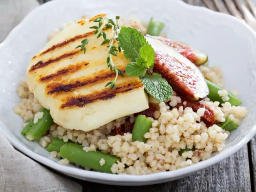 Kuskus z grillowanym serem halloumi, fasolką szparagową i figami, ozdobiony miętą.
