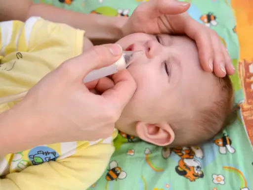 Mani che usano un aspiratore nasale per un neonato con raffreddore. Il piccolo indossa una tutina gialla con disegni di animali.