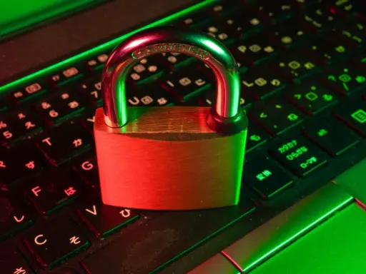 Un cadenas sur un clavier d'ordinateur, symbolisant la **sécurité informatique**. La lumière rouge et verte crée une ambiance de protection numérique.