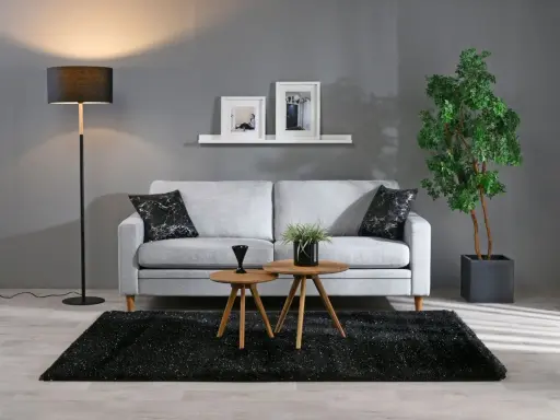 En stilren inredning grått med en ljusgrå soffa, svart matta och en golvlampa. Två runda bord framför soffan.