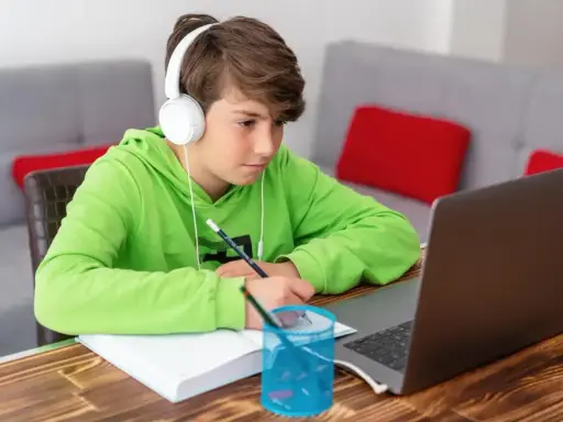 Chłopiec w słuchawkach uczy się zdalnie, notując w zeszycie. Zastanawia się, ile kosztują studia, gdy widzi ceny kursów online.