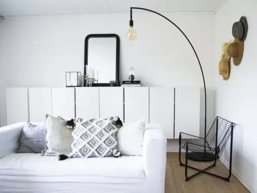 En stilren och modern manlig inredning med vit soffa, svarta detaljer och en golvlampa.