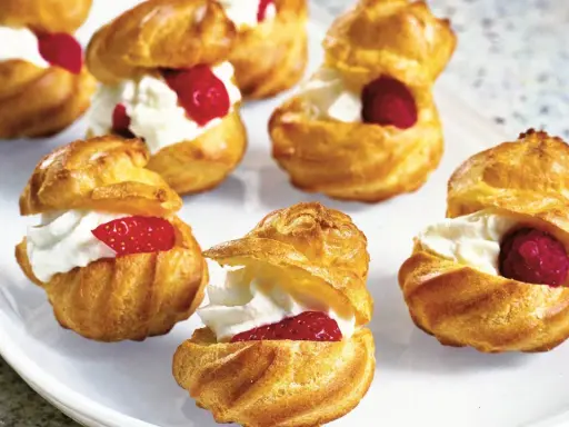 Små petit choux fyllda med vispgrädde och toppade med hallon eller jordgubbar. En härlig dessert!