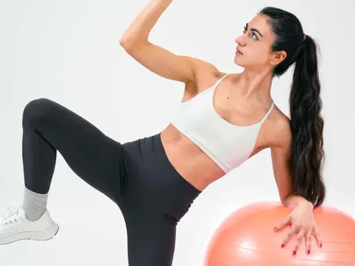 Frau macht Übungen mit Gymnastikball. Sie fragt sich, was ist Kreatin, während sie ihre Muskeln trainiert.