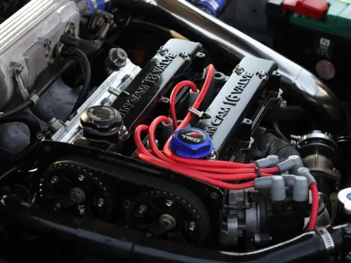 Motor de coche con tapa de válvulas "16 VALVE", cables rojos y correa de distribución.