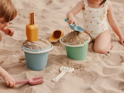 Niños disfrutando de juegos en la playa con cubos y palas de arena.