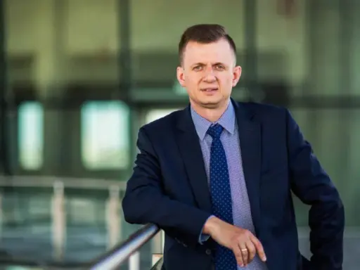 Mężczyzna w garniturze i krawacie opiera się o barierkę.