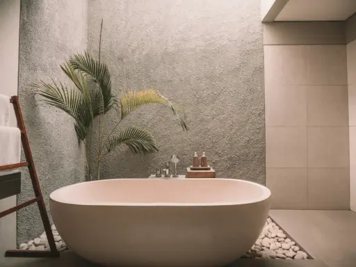 Elegante bañera exenta, rodeada de piedras blancas y una planta tropical. Muestra varios tipos de bañeras para un baño de lujo.