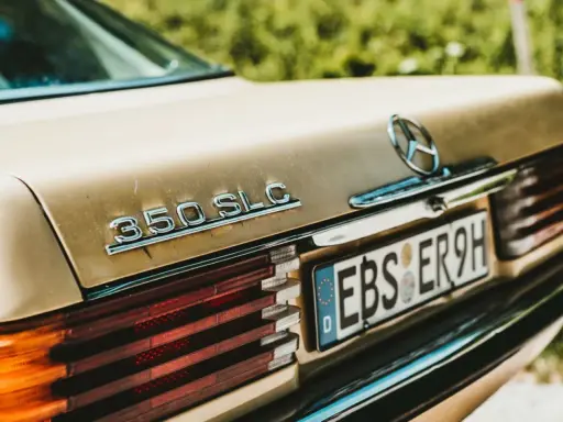Detalle de un Mercedes 350 SLC dorado, con la luz de matrícula visible, listo para pasar la ITV.
