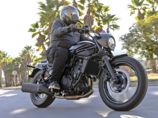 Mężczyzna w kasku jedzie czarnym motocyklem Kawasaki EN 500. Wady i zalety tego modelu są dyskutowane podczas jazdy wśród palm.