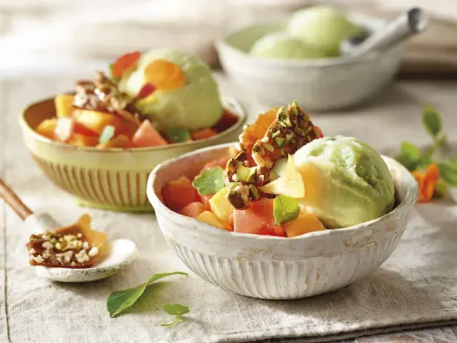Deliciosos postres saludables: helado verde cremoso con trozos de melón, papaya y un toque crujiente de pistachos.