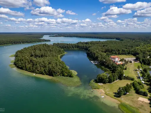 Malownicze jezioro Urszulewskie otoczone lasem, z hotelem i polem namiotowym na brzegu.