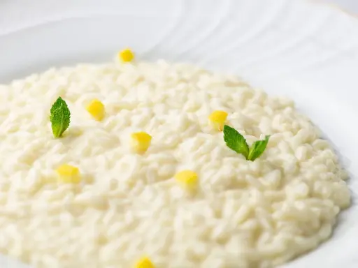 Un cremoso risotto al limone, guarnito con cubetti di limone e foglie di menta fresca, pronto per essere gustato.