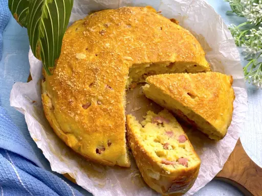 Una deliziosa torta salata prosciutto e formaggio, dorata e soffice, con una fetta tagliata per mostrare il ripieno.