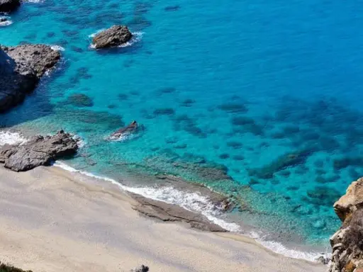 Spiaggia dorata e mare cristallino con scogli a Capo Cozzo.
