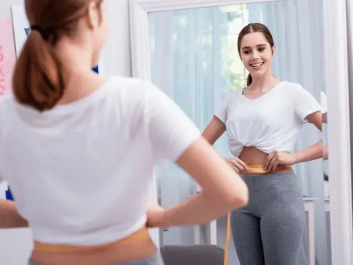 Mujer se mide la cintura con cinta métrica, sonriendo al verse en el espejo. No hay evidencia de que el diu de cobre engorde.