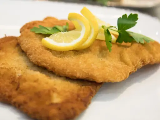 Zwei goldbraune Schnitzel, perfekt in Butter gebraten, garniert mit Zitronenspalten und Petersilie auf einem weißen Teller.