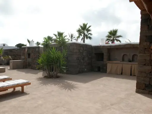 Un cortile in cemento trasformato con piante rigogliose, un barbecue in pietra e comodi lettini. Idee per come abbellire un cortile in cemento.