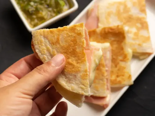Ciepłe quesadille z szynką i serem, idealne na szybką kolację. Obok sos.