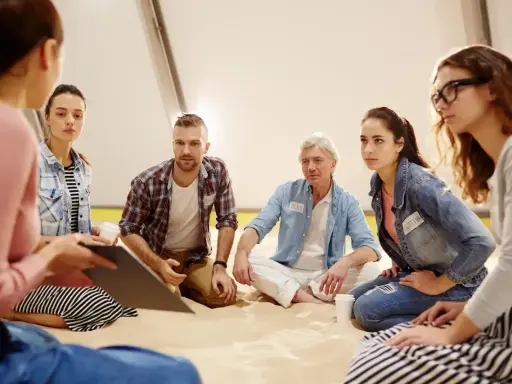 Grupa ludzi na sesji psychoterapii grupowej yalom. Siedzą w kręgu, słuchając siebie nawzajem.