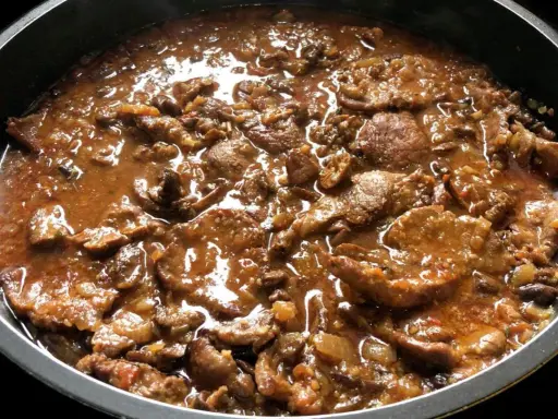 Fricandó de ternera cocinándose en una sartén, con trozos de carne tierna en una salsa espesa y aromática.