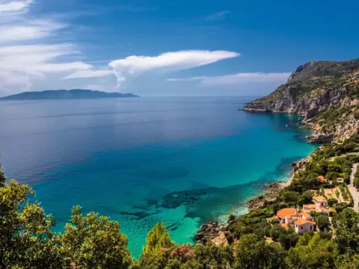 Un angolo di paradiso dove in Toscana c'è il mare. Acque cristalline lambiscono una costa rocciosa, con case dai tetti rossi immerse nel verde.