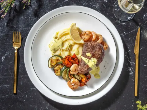 Ein köstliches Surf and Turf Rezept: saftiges Steak, Garnelen, Kartoffelpüree und gegrilltes Gemüse auf einem Teller.