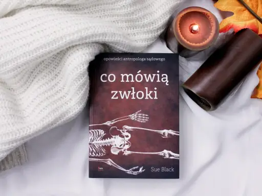 Książka "Co mówią zwłoki" Sue Black, opowieści antropologa sądowego, leży obok zapalonej świecy i jesiennych liści.