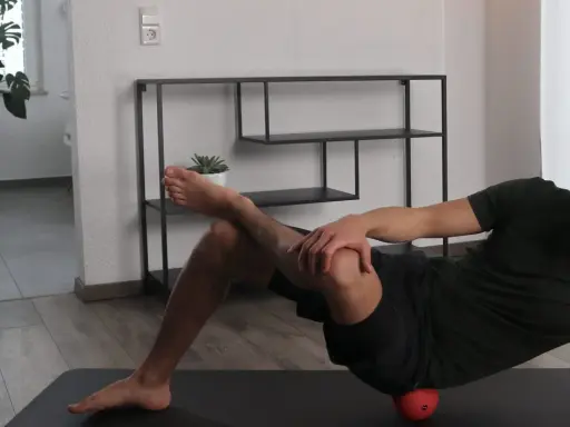 Mann dehnt den Piriformis mit einem roten Ball unter der Hüfte.