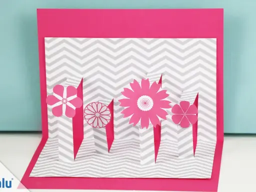 Eine pinke Pop-up-Karte basteln mit Blumen auf grau-weißem Zickzack-Muster.