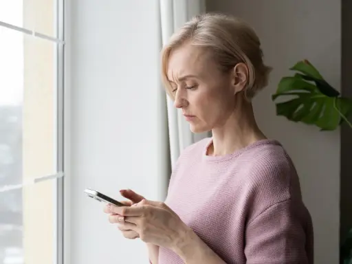 Besorgte Frau blickt auf ihr Handy. Sie fragt sich, ob ihr Handy ausspioniert wird.