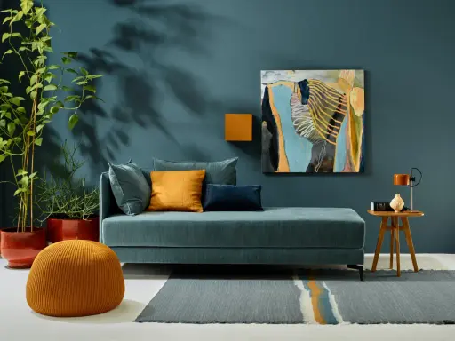 Ein Wohnzimmer mit einem türkisfarbenen Sofa, orangefarbenen Akzenten und einem abstrakten Gemälde. Die Wandfarbe könnte die Farbe des Jahres 2026 sein.
