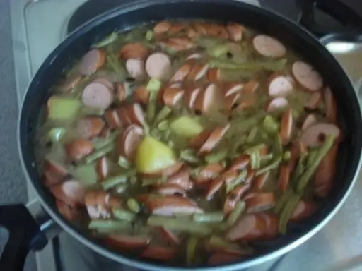 Ein deftiges schnippelbohnen rezept mit Kartoffeln und Würstchen in einer Pfanne.