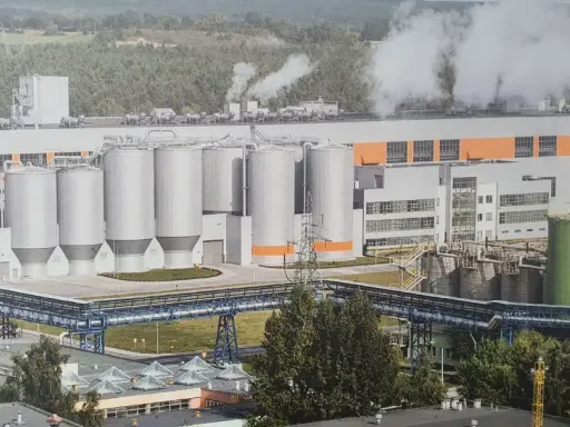 Ogromna fabryka celulozy w Polsce z wieloma silosami i rurociągami, z której unosi się para.