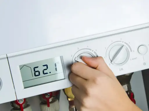 Dłoń reguluje ustawienie pieca gazowego. Na wyświetlaczu 62.1°C, obok manometr i pokrętła regulacji.
