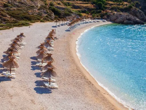 Rządki parasoli i leżaków na kamienistej plaży, obok krystalicznie czystej, turkusowej wody. To jedna z najpiękniejszych plaż w Europie, idealna na relaks.