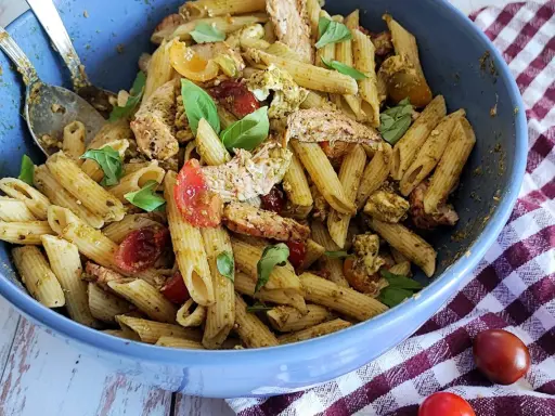 Un plat généreux de penne à la salade pesto, garni de poulet effiloché, tomates cerises et basilic frais. Un délice pour les papilles !