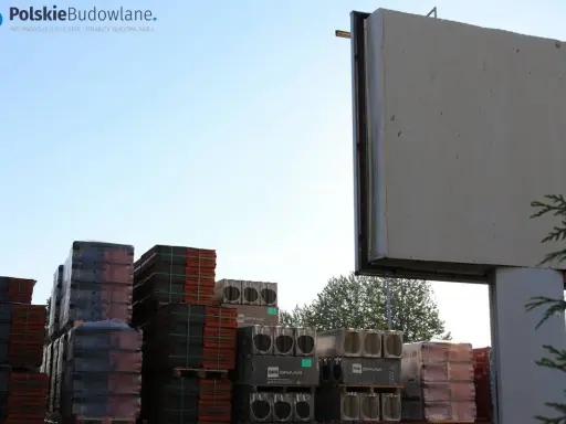 Stosy dachówek i materiałów budowlanych pod pustym billboardem. Reklama na budynku inaczej, czekająca na nowe hasło.